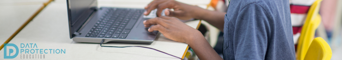 A child working on a laptop in a classroom with other children doing the same. Data Protection Education logo in the bottom right of the picture