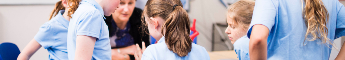 School children wearing blue shirts and grey skirts in a class room